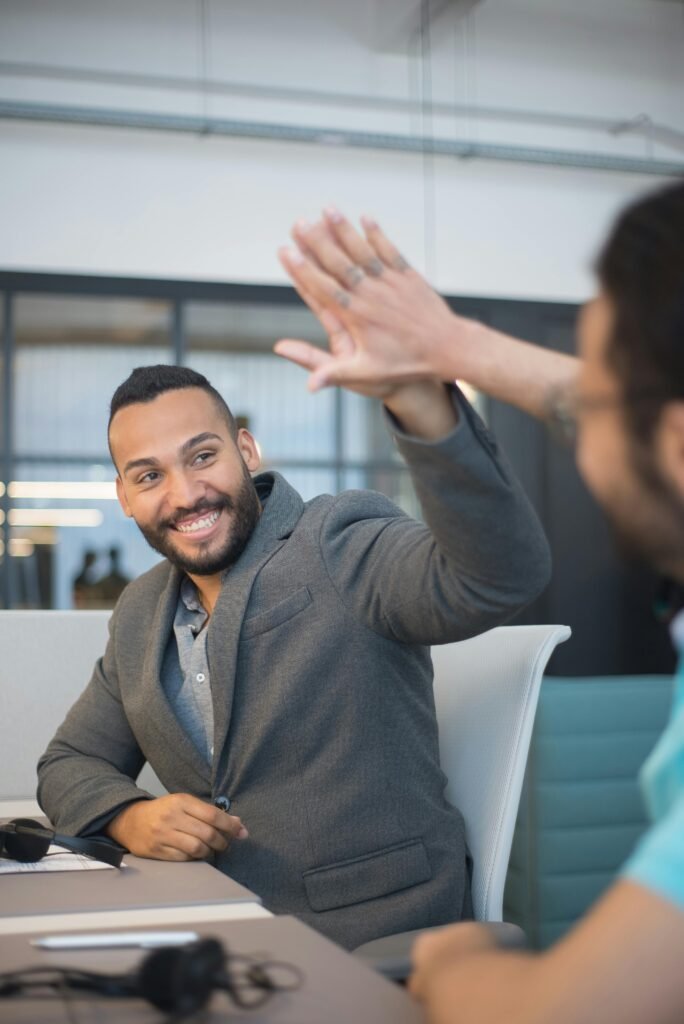 Smiling colleagues share a high-five in a modern office environment, showcasing teamwork and success.
